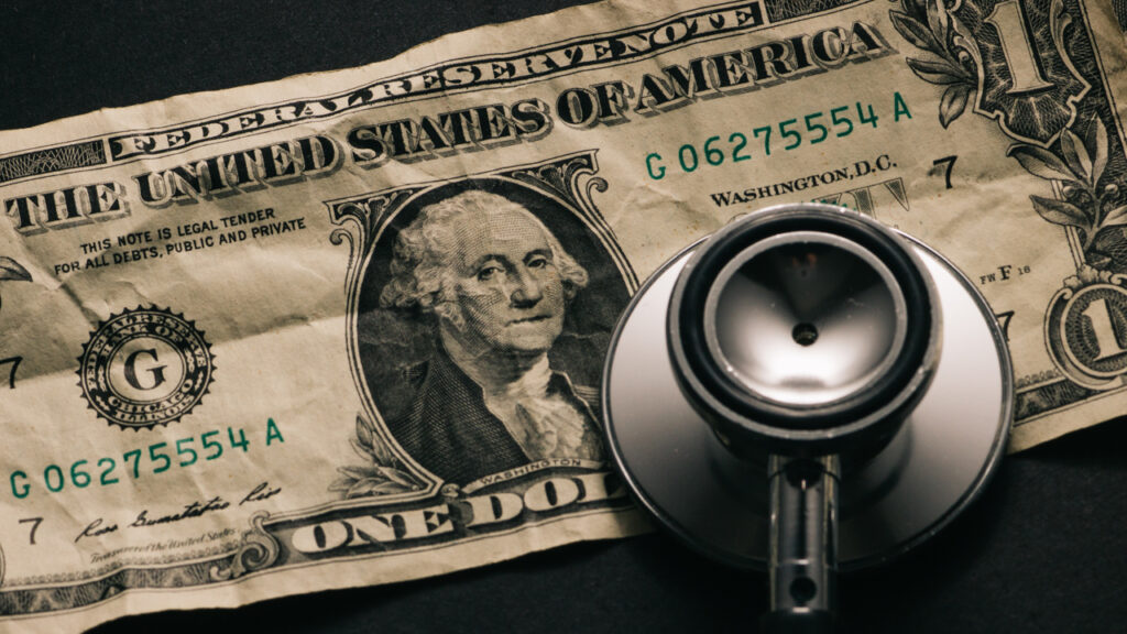 Dollar bill and medical supplies with prescription medical pills and doctors health care stethoscope.